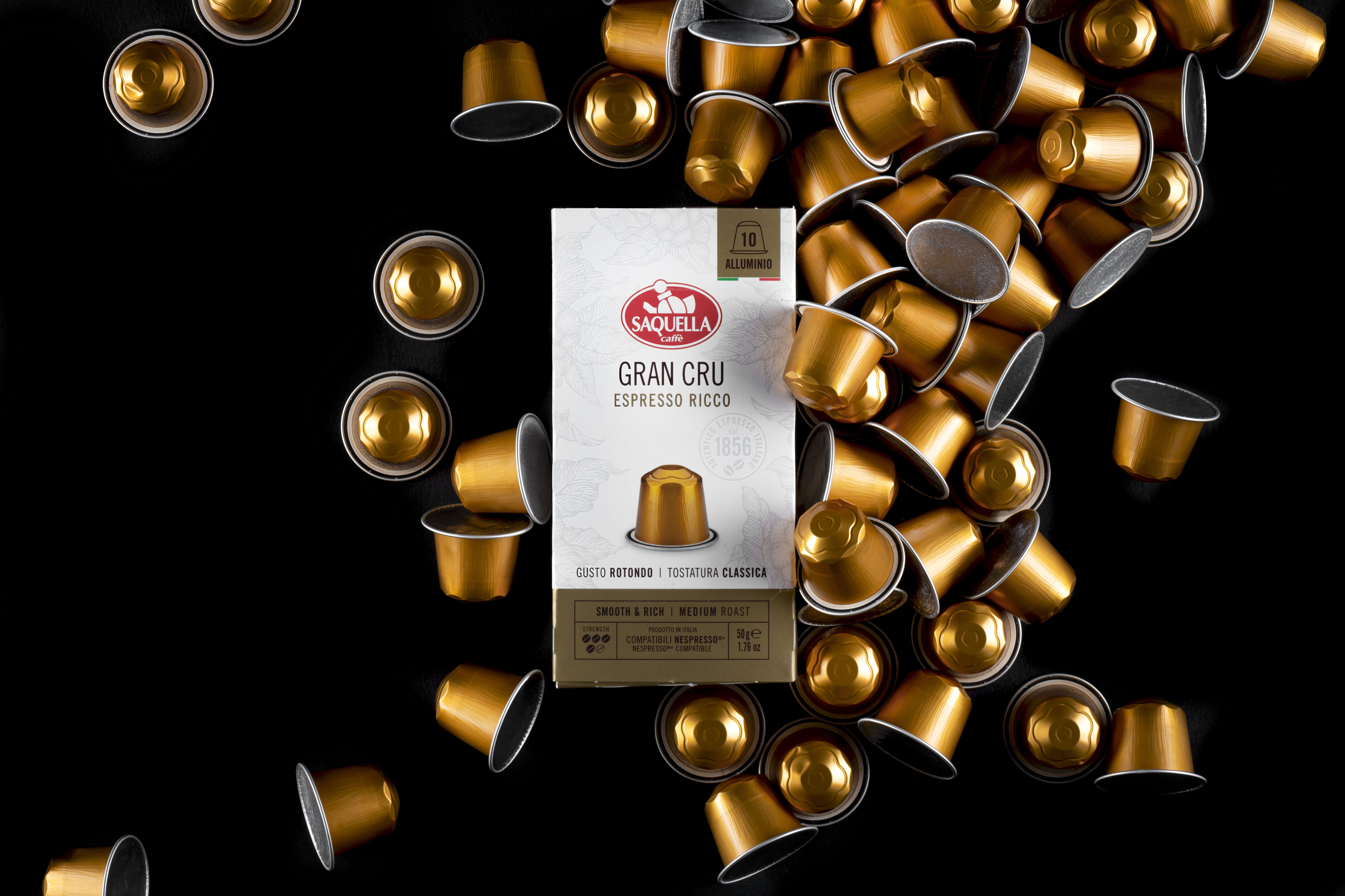 Eleganckie, złote kapsułki z kawą Saquella Gran Cru Espresso Ricco na czarnym tle – przykład wysokiej jakości włoskiej kawy do ekspresów kapsułkowych, idealnej do nowoczesnego biura, które stawia na komfort, wygodę i prestiż