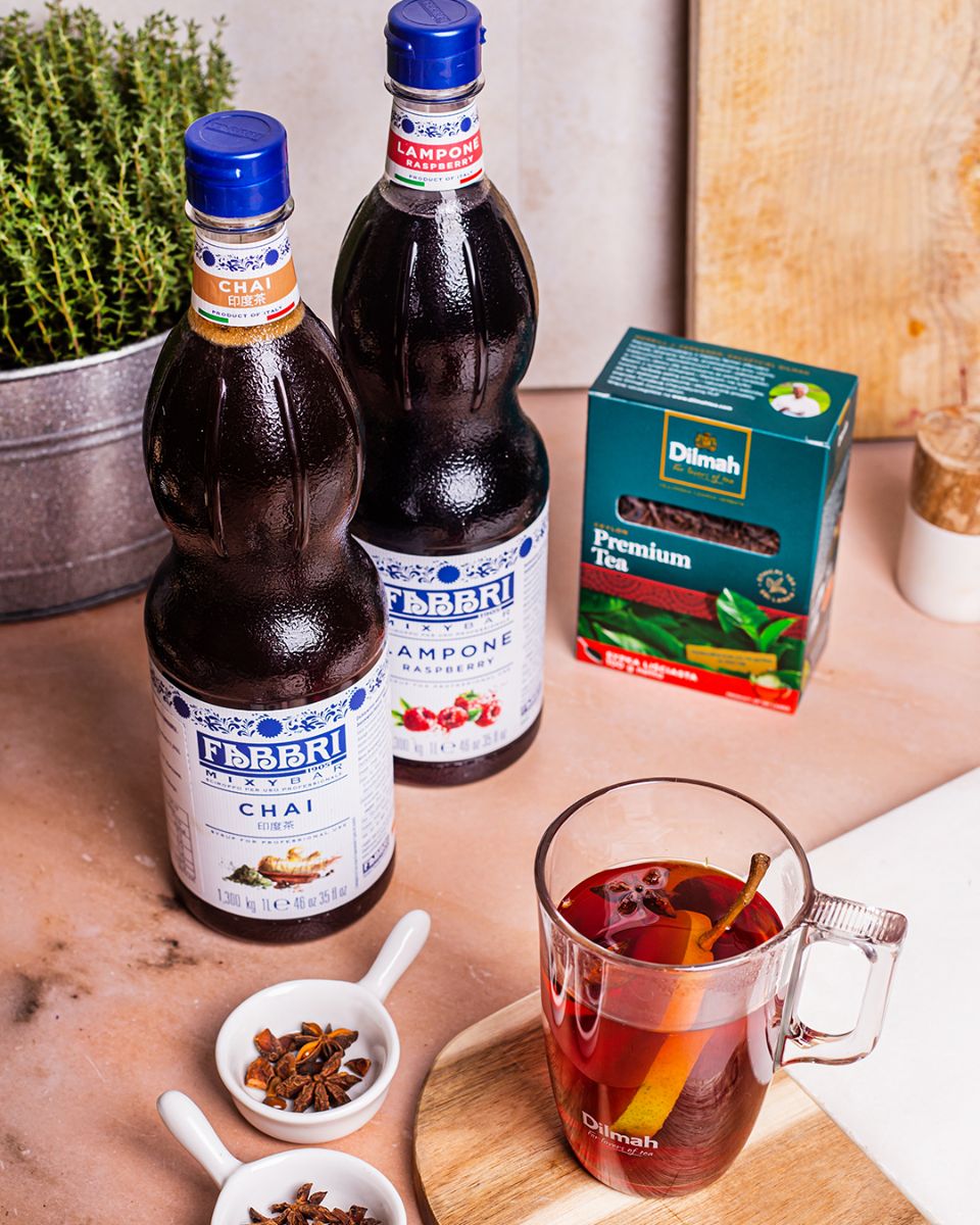 Butelka syropu Fabbri Mixybar Chai obok innych dodatków do herbaty – anyżu, syropu Fabbri Mixybar Lampone oraz paczki z herbatą sypaną Dilmah. W kubku herbata z gruszką, syropami i anyżem.