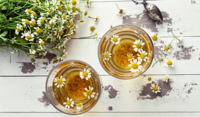 Dwie filiżanki z naparem z rumianku Dilmah Pure Camomile, udekorowane jadalnymi kwiatami rumianku.